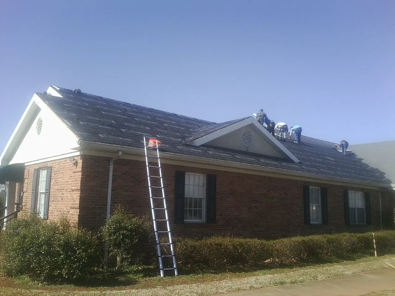 Crew tearing shingles off a brick ranch roof with a ladder set — Emergency Roof Repair work by our crew in Centreville