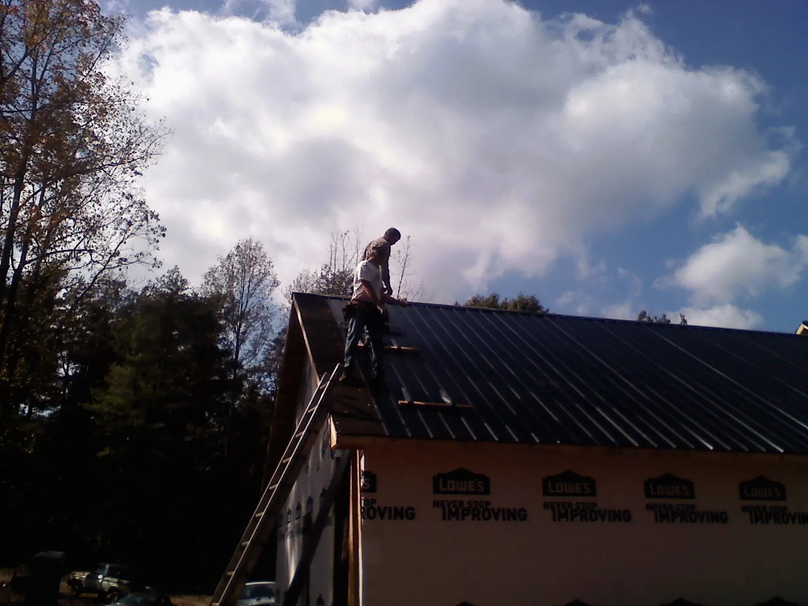 Roofer fastening dark metal panels high against a cloudy sky, from a Roof Inspection job in Centreville