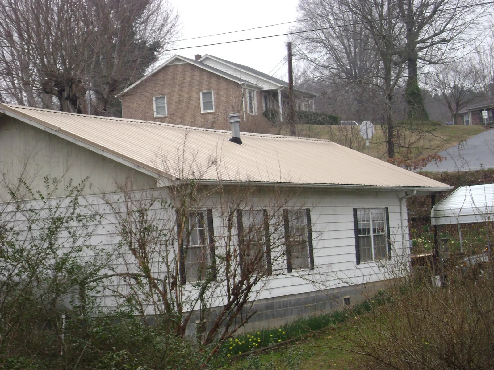 Tan metal roof on a white sided house set into a hillside — Commercial Roofing by Roofing Brothers in Centreville